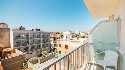 Utsikt fra en balkong som viser et boligområde med bygninger og trær under en klar blå himmel. (AI-generert tekst)