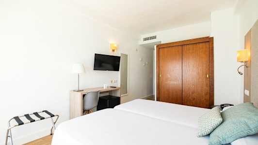 Hotellrom med to enkeltsenger, skrivebord, stol, TV og garderobeskap. (AI-generert tekst)