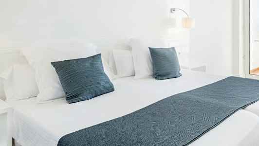 Hvitt sengetøy på en dobbeltseng med blå pynteputer og sengeteppe. (AI-generert tekst)