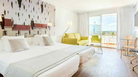 Et hotellrom med to enkelt oppredde senger, en grønn sofa og en balkong i bakgrunnen. Veggdekorasjonen har et kunstverk med uvanlig design. (AI-generert tekst)