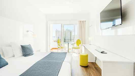 Lyst hotellrom med dobbeltseng, TV på veggen og sittemøbler ved vinduet. (AI-generert tekst)