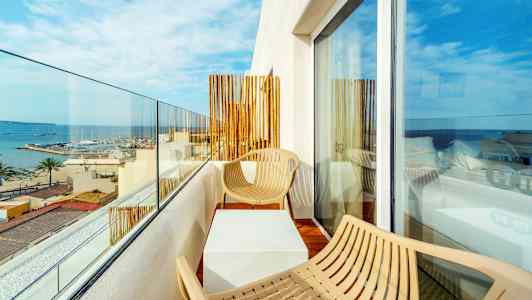 Balkong med to stoler og et bord, utsikt over sjøen og en marina. (AI-generert tekst)