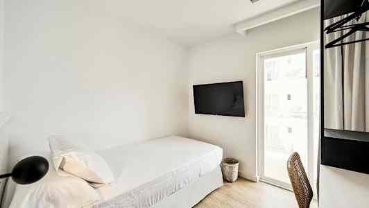 Et hotellrom med en enkeltseng, veggmontert TV og et skrivebord med stol ved siden av et vindu. (AI-generert tekst)