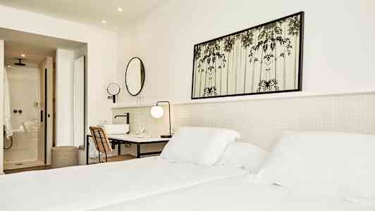 Lyst hotellrom med seng, skrivebord og bad. (AI-generert tekst)