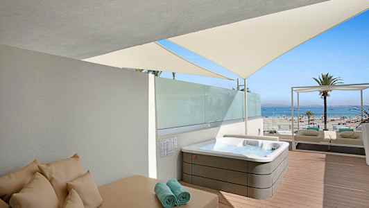 Et soldekk med en jacuzzi, solseng og utsikt mot stranden og havet. (AI-generert tekst)