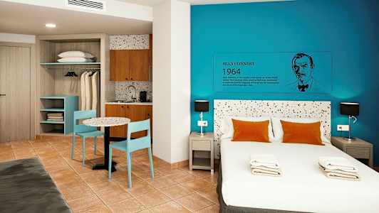 Et moderne hotellrom med en dobbeltseng, blå vegger og en liten kjøkkenkrok. (AI-generert tekst)