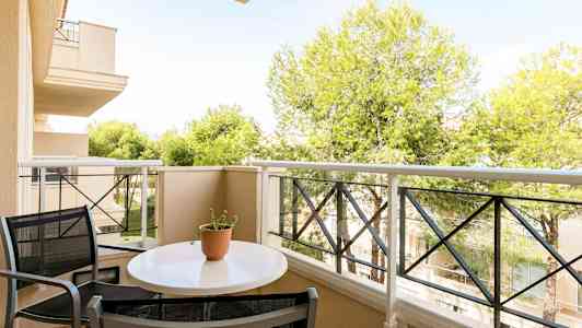 En balkong med et bord og stoler, samt utsikt over trær og bygninger. (AI-generert tekst)