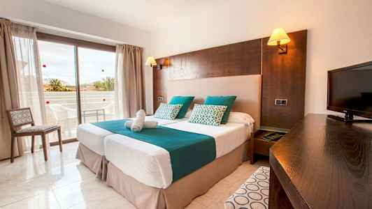 Et hotellrom med to enkeltsenger, en TV og en balkong i bakgrunnen. (AI-generert tekst)