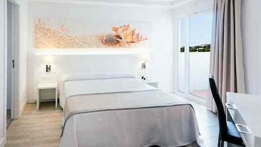 Et hotellrom med dobbeltseng, hvitt og beige interiør, dekorasjon med skjell over sengen. (AI-generert tekst)