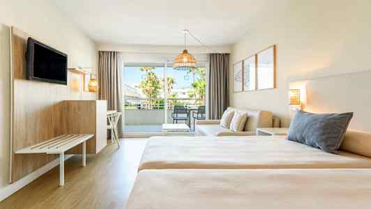 Et hotellrom med to senger, en sittegruppe og balkong med utsikt. (AI-generert tekst)