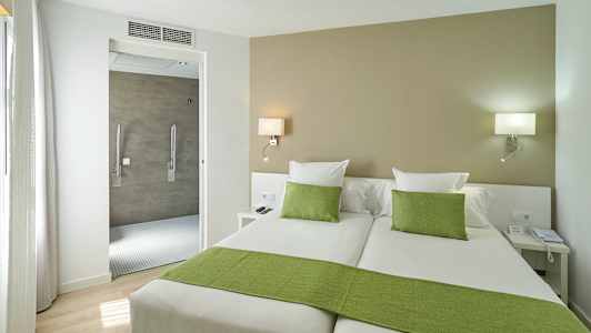 Hotellrom med to enkeltsenger, grønt sengetøy og en åpning mot badet. (AI-generert tekst)