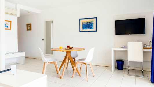 Et lyst rom med et rundt spisebord og stoler, en TV på veggen og en arbeidsplass med en stol. (AI-generert tekst)