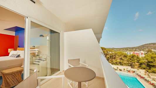 Utsikt fra en balkong med bord og stoler, med et basseng og bygninger i bakgrunnen. (AI-generert tekst)