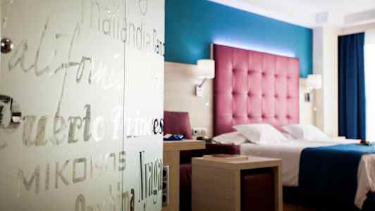 Hotellrom med fargerik innredning, seng og bord. (AI-generert tekst)