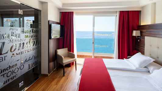 Et hotellrom med store senger, rød innredning og en balkong med utsikt over havet. (AI-generert tekst)