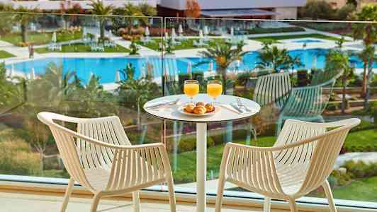 To stoler ved et bord med frokost i et rom med utsikt over bassengområdet. (AI-generert tekst)