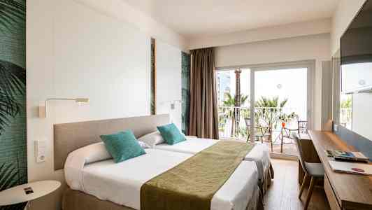 Hotellrom med to enkeltsenger, skrivebord og balkong med utsikt mot palmer. (AI-generert tekst)