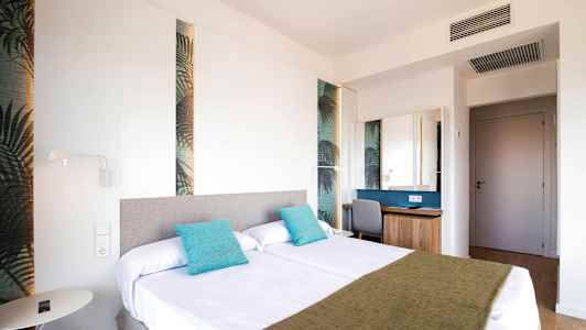 Et hotellrom med to senger dekorert med turkise puter og et grønt sengeteppe. (AI-generert tekst)