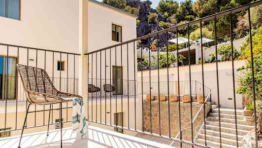 En balkong med en stol og et rekkverk, omgitt av en bygning og grøntområder. (AI-generert tekst)