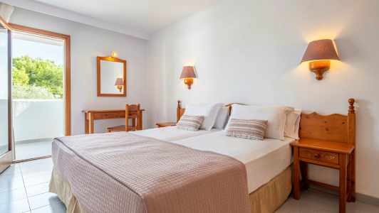 Et hotellrom med en dobbeltseng, to sengelamper, et skrivebord, en stol og en balkong. (AI-generert tekst)