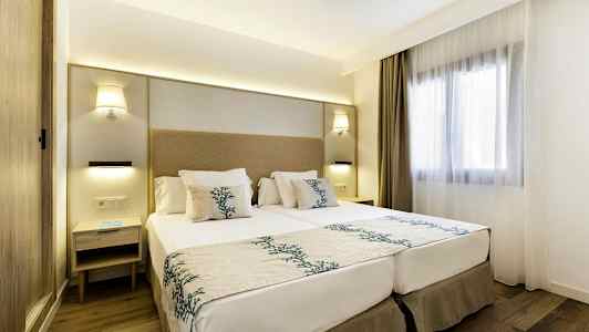 Moderne innredet hotellrom med en dobbeltseng, nattbord og et vindu med lyse gardiner. (AI-generert tekst)