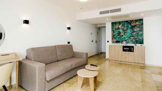 Lys leilighet med grå sofa, skrivebord og kjøkkenkrok. (AI-generert tekst)