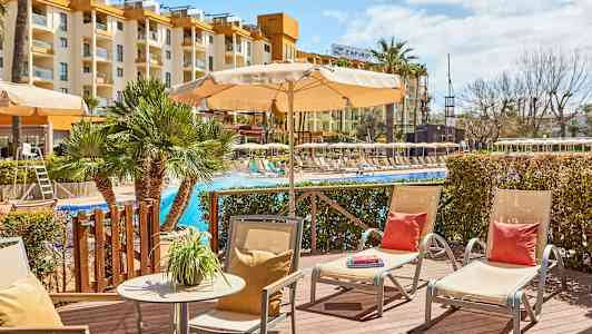 Utendørsområde ved basseng med solsenger og parasoller, hotellbygning i bakgrunnen. (AI-generert tekst)