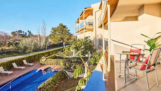 En balkong med bord og stoler, samt utsikt mot bassengområde og hage. (AI-generert tekst)