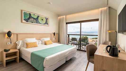 Bilde av et hotellrom med dobbeltseng, skrivebord og utsikt mot sjøen. (AI-generert tekst)