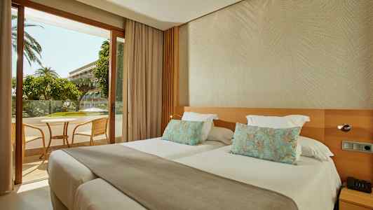 Hotellrom med to separate senger og utsikt mot en møblert balkong. (AI-generert tekst)