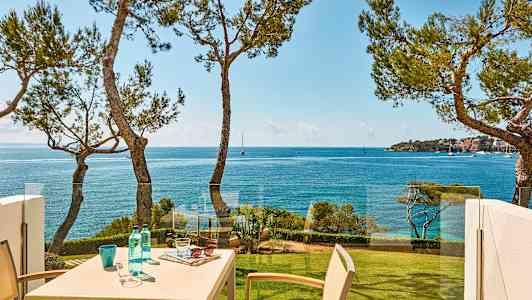 En utsikt over havet med et bord på en balkong, omgitt av trær. (AI-generert tekst)