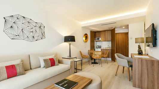 Et lyst og moderne hotellrom med sitteområde, skrivebord, sofa og en liten kjøkkenkrok. (AI-generert tekst)