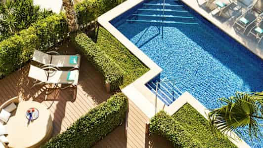 Et bassengområde med solsenger og grønne busker. (AI-generert tekst)