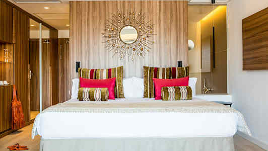 Moderne hotellrom med en stor seng, dekorative puter i ulike farger og trepanel på veggen bak. (AI-generert tekst)