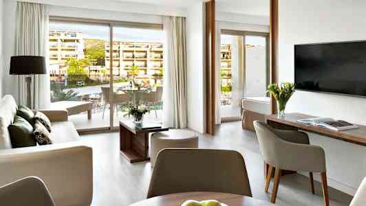 Moderne innredet hotellsuite med sittegruppe, bord og balkong. (AI-generert tekst)