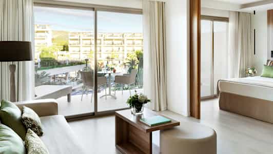 Utsikt fra et hotellrom mot en balkong og et utendørsområde med basseng og bygninger. (AI-generert tekst)