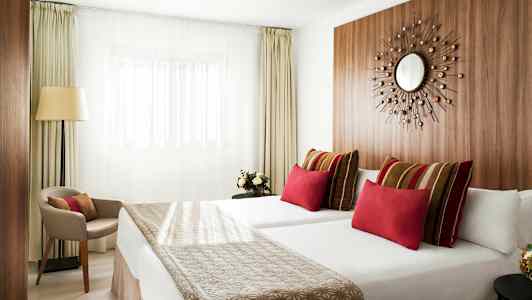 Moderne hotellrom med to senger, fargerike puter og minimalistisk innredning. (AI-generert tekst)