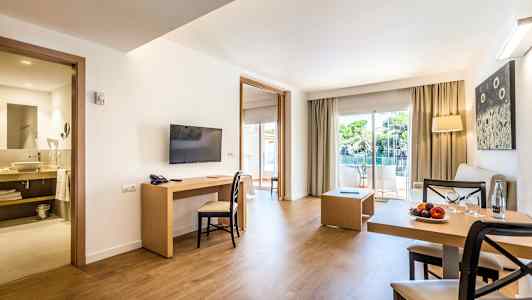 En moderne hotellsuite med sittegruppe, spisebord, TV og utgang til balkong med utsikt. (AI-generert tekst)