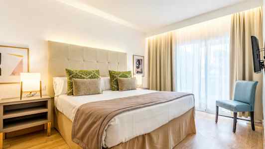 Et hotellrom med en dobbeltseng, sidebord, stol og stort vindu. (AI-generert tekst)