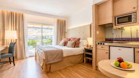 Et hotellrom med en stor seng, skrivebord og kjøkken, samt en balkong med utsikt. (AI-generert tekst)