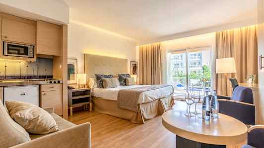 Hotellrom med dobbeltseng, sittegruppe og kjøkken, samt balkong med utsikt. (AI-generert tekst)