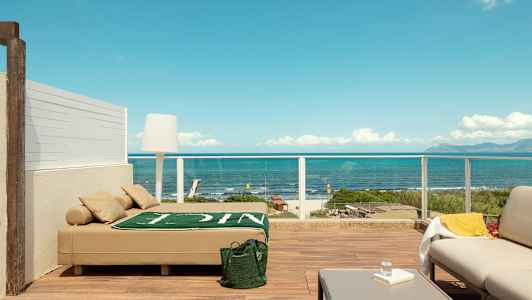 Terrasse med moderne møblering og utsikt over havet, inklusive en solseng, sofamøbler og bord. (AI-generert tekst)