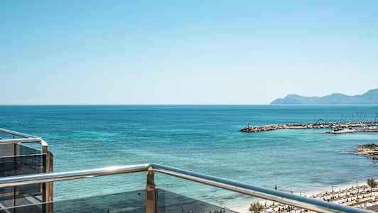 Utsikt fra en balkong mot havet og en strand med parasoller. (AI-generert tekst)