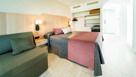 Et hotellrom med dobbeltseng, sofa og åpen garderobe. (AI-generert tekst)