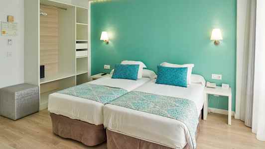 Et hotellrom med to enkeltsenger, turkise puter og vegger. (AI-generert tekst)