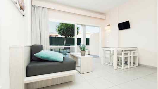 Et moderne lyst rom med sittemøbler, bord og en plante, store vinduer og hageutsikt. (AI-generert tekst)