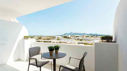 Balkong med bord og stoler, utsikt over omkringliggende bygninger og fjell. (AI-generert tekst)