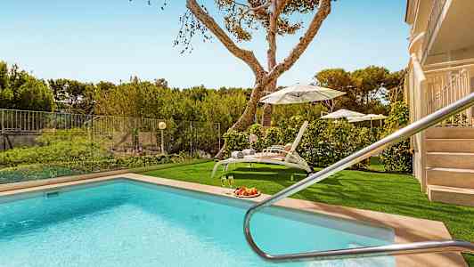 Utendørs basseng med solsenger og parasoller samt grøntområder i bakgrunnen. (AI-generert tekst)