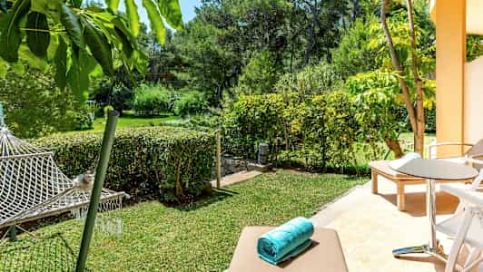 En terrasse med solsenger og sittegruppe, utsikt over en hage med hengekøye. (AI-generert tekst)