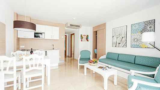 Bildet viser en lys og moderne møblert stue med et kjøkkenområde og spiseplass. (AI-generert tekst)